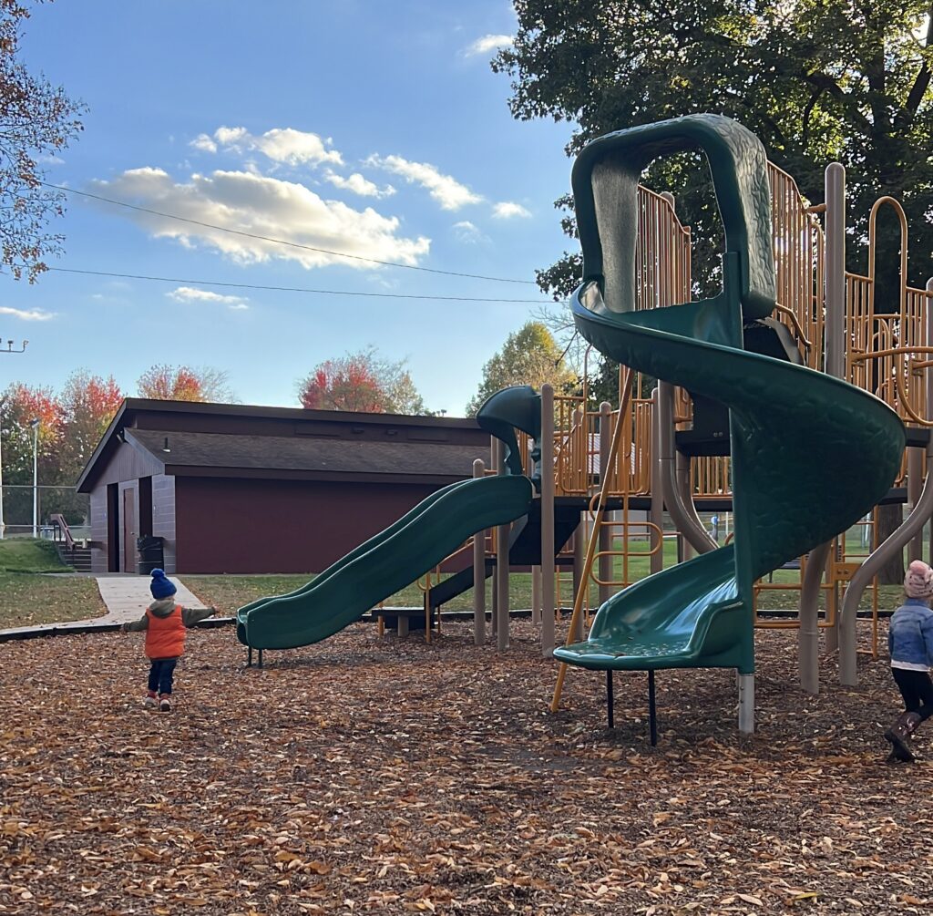 two children play at a playground in the fall.