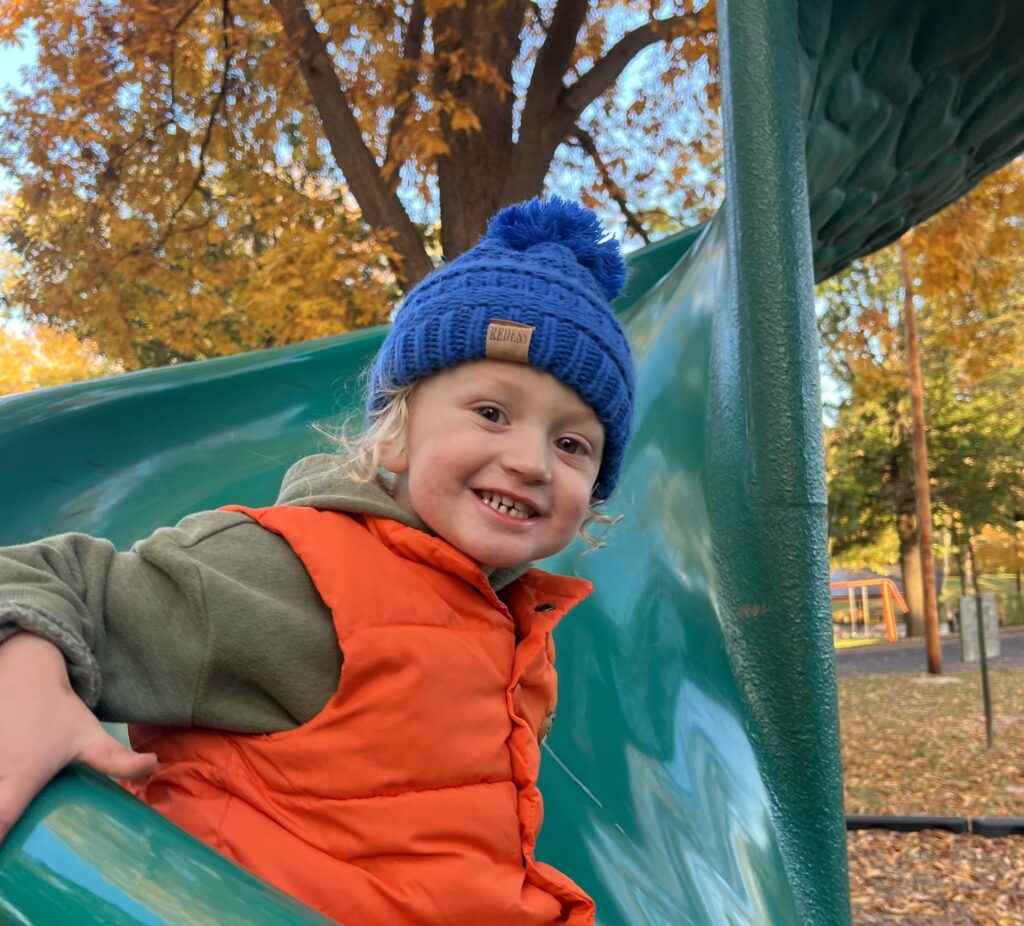a young child smiles sliding down a green slide. 